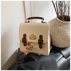 Detail of cream backpack with puppy embroidery and clear window filled with pom-poms
