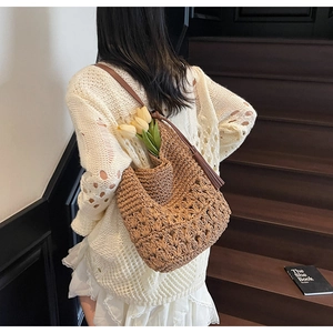 Detail of woven straw hobo bag featuring dark leather strap and long fringe tassel