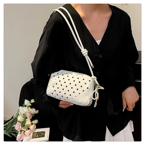 Close-up of white polka dot crossbody bag with pearl charm and embossed letter B detail