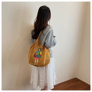 Detailed back view of a yellow hollow knit tote bag with a cartoon embroidery on a shoulder strap