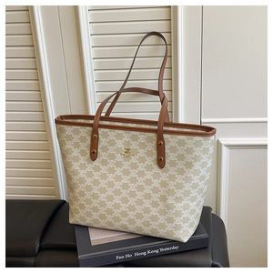 Close-up of beige patterned tote bag with gold logo and brown leather handles on books