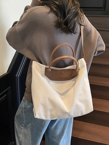 Large beige canvas tote bag with brown leather handles and adjustable strap for women