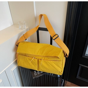 Detail of yellow nylon tote bag with dual front pockets atop a black suitcase