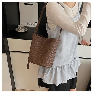 Detail of dark brown woven bucket bag with adjustable strap shown on model in street style
