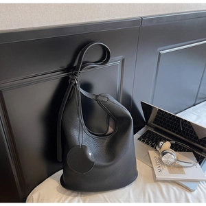 Detail of black pebbled leather bucket tote with shoulder strap and circular pendant