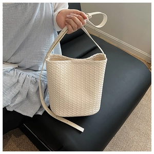 Detail of cream woven bucket bag with checkered texture and adjustable shoulder strap