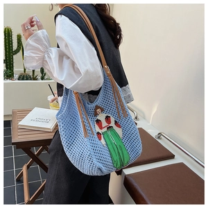 Detail of light blue knit tote bag with strawberry patch and brown leather strap
