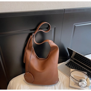 Detailed macro of brown leather tote bag with lychee texture and adjustable strap on bed