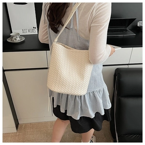 Detailed view of the woven texture and leather strap on a beige bucket bag worn by model