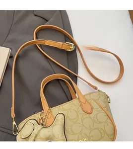 Detail der beigen Monogramm-Handtasche mit braunen Ledergriffen und goldenen Metallteilen