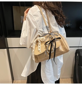 Dettaglio borsa a tracolla beige lucida con fiocchi di pizzo, nastri e tasche frontali