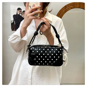 Detail of black polka dot handbag featuring a metal heart charm and a pearl strap detail