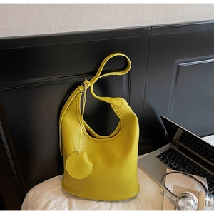 Detail of a bright yellow lychee leather tote bag with round charm and adjustable strap