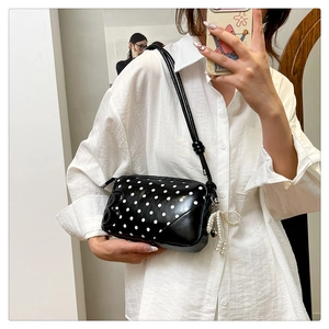 Polka dot crossbody bag detail featuring a pearl bow pendant and glossy leather texture