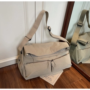 Detail of light khaki multi-pocket crossbody bag with wide strap on wooden floor