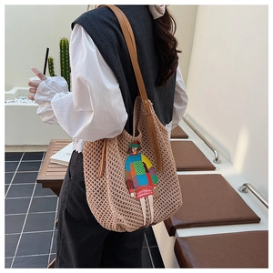 Close-up of beige knitted tote bag with artistic cartoon embroidery and leather strap