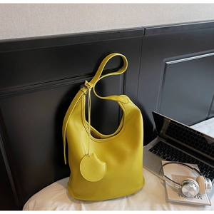 Detail of yellow lychee-textured leather tote bag with round charm in a cozy setting