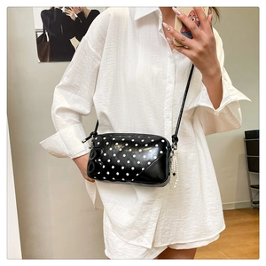 Detailed side view of black polka dot crossbody bag with 8-shaped charm and pearl detail