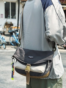 Neutral color-block nylon messenger bag with wide shoulder strap in city street scene