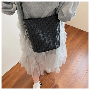 Detail of black woven bucket bag showing premium leather texture on a model shoulder