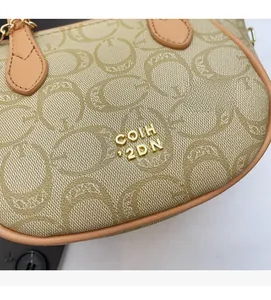 Detail der beigen Jacquard-Handtasche mit Prägemuster und goldenem Metall-Logo-Schild