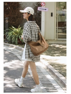 Brown canvas crossbody bag with wide strap shown on a model in an outdoor street setting