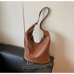 Close-up of brown pebbled leather tote bag with side metal buckle and round tag detail