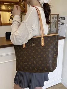 Classic dark brown monogram tote bag with gold logo shown in a cozy cafe setting