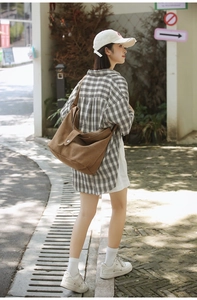 Detail of a large brown canvas crossbody bag with metal snap closure in a street setting