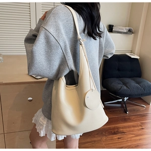 Close-up of beige litchi grain leather bucket bag worn by model in a minimalist setting