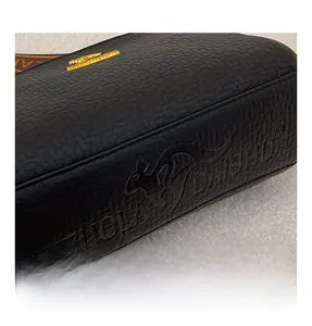 Close-up of litchi grain texture on Boston bag with embossed logo and golden metal hardware
