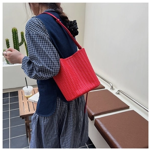 Detail view of the red woven bucket bag showing the crossbody strap in a lifestyle setting