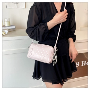 Detail of pink polka dot crossbody bag with pearl charm and embossed letter B accent