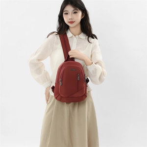 Détail du sac à dos bandoulière en nylon rouge foncé avec plusieurs poches sur le modèle