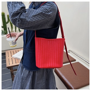 Red woven bucket bag with fine shoulder strap shown in a modern lifestyle setting