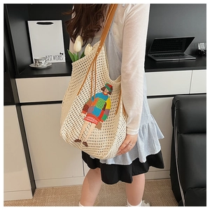 Detail view of a beige knit tote bag with art embroidery on a female model shoulder