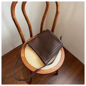 Detailed view of deep brown woven leather bag texture on a vintage wooden chair