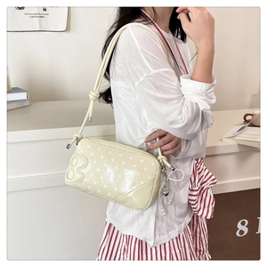 Close-up of creamy yellow polka dot shoulder bag with pearl heart charm and 'B' detail