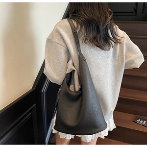 Detailed view of large black lychee leather tote bag worn with casual outfit on stairs