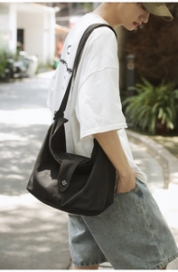 Detail of black canvas crossbody bag with silver decorative buckle worn by a model outdoors