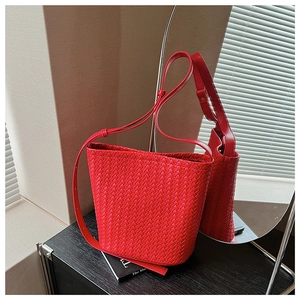 Detail view of red woven bucket bag with fine shoulder strap on a black reflective surface