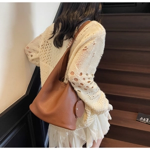 Detail of caramel brown litchi pattern leather bucket bag with round charm and strap