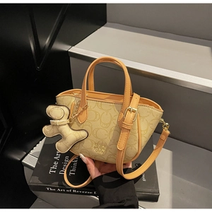 Detailansicht der beigen Handtasche mit C-Muster, orangefarbenem Rand und Bärenanhänger