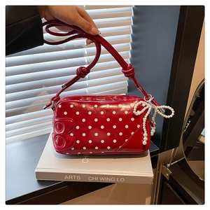 Close-up of red polka dot patent leather crossbody bag with a pearl bow charm detail