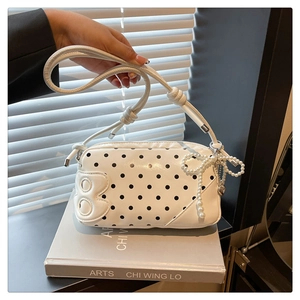 Detail of white polka dot crossbody bag with B leather patch and pearl bow pendant