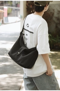 Detail of black canvas crossbody bag with silver metal buckle on outdoors model