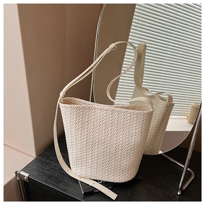 Detail of beige woven leather bucket bag featuring intricate criss-cross texture and strap