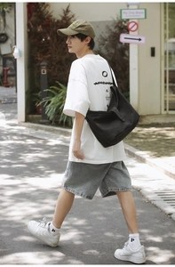 Detail view of large black canvas crossbody bag shown on a model in a street style setting
