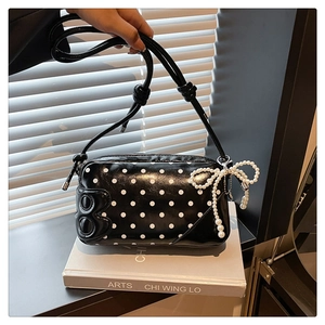 Close-up of a glossy black polka dot shoulder bag with a beaded bow and letter B detail