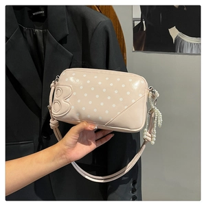 Close-up of a pink polka dot handbag featuring a B-shaped patch and pearl tassel detail